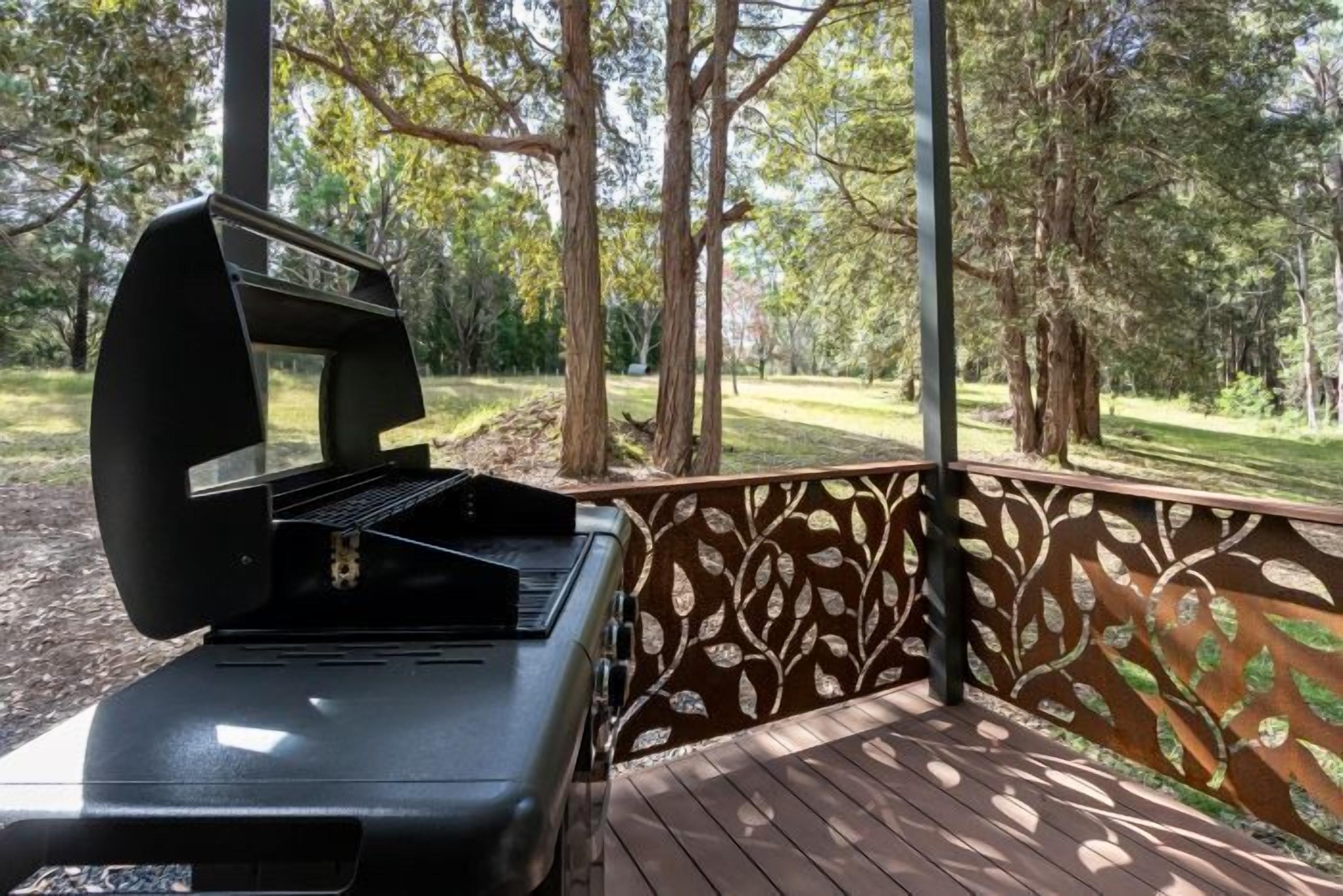 Una parrilla para barbacoa en una terraza de madera con una pared decorativa con motivos de hojas.