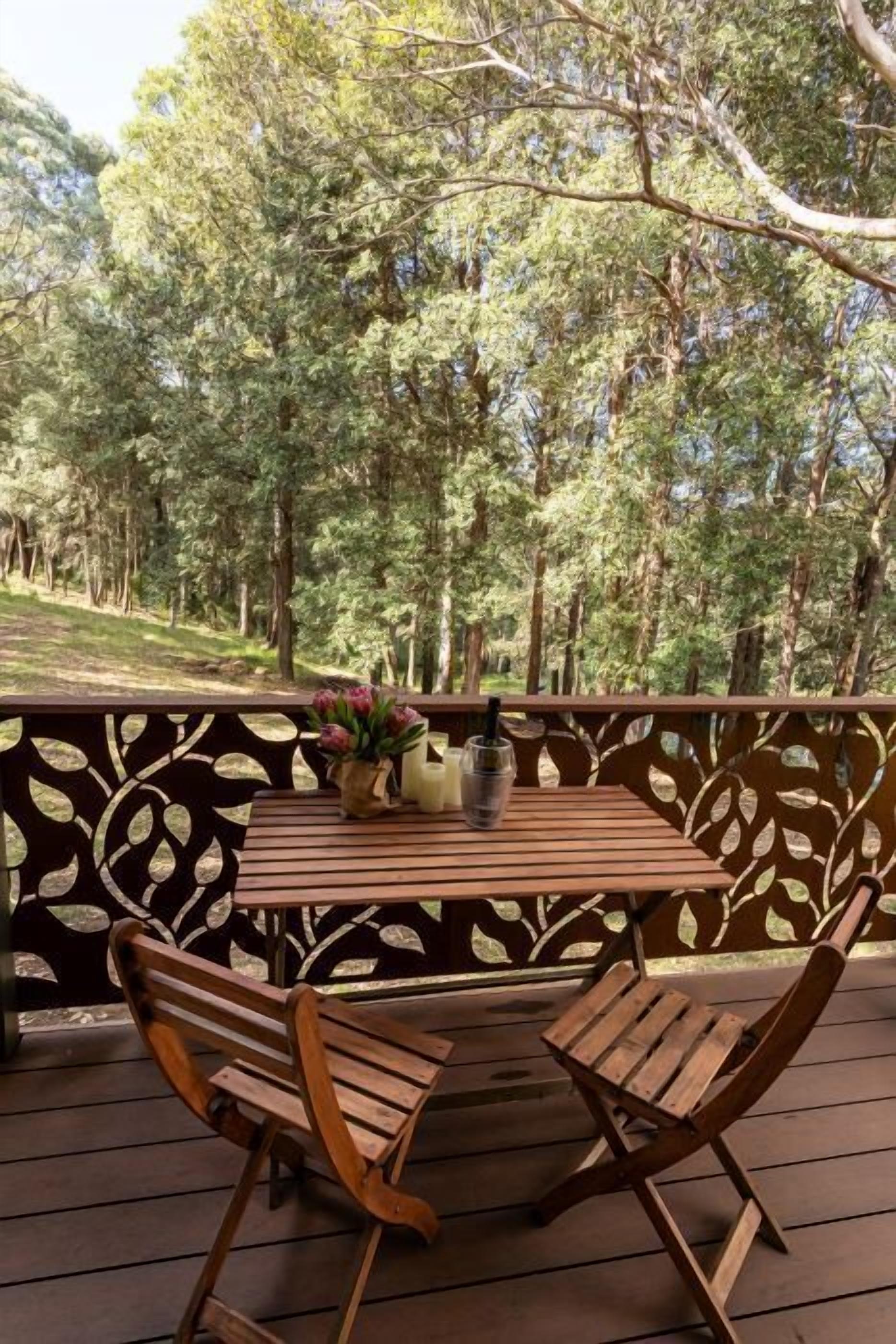 Eine Holzterrasse im Freien mit Tisch und Stühlen, umgeben von einem dekorativen Zaun mit Blattmustern.