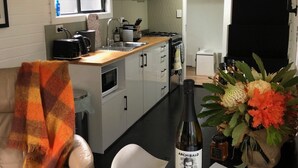 Une cuisine compacte équipée d’une cuisinière, d’un évier et d’un petit coin repas. On y trouve un lit superposé sur lequel est posé un ours en peluche.