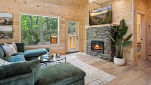L’intérieur chaleureux d’un chalet en bois avec une cheminée en pierre, de grandes fenêtres et un coin salon confortable.