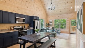 Une cuisine moderne avec des meubles de couleur sombre, une table en bois et un banc. Une grande fenêtre offre une vue sur la verdure à l’extérieur.