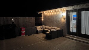 An outdoor seating area with a sofa and a table, a wooden fence, and string lights.