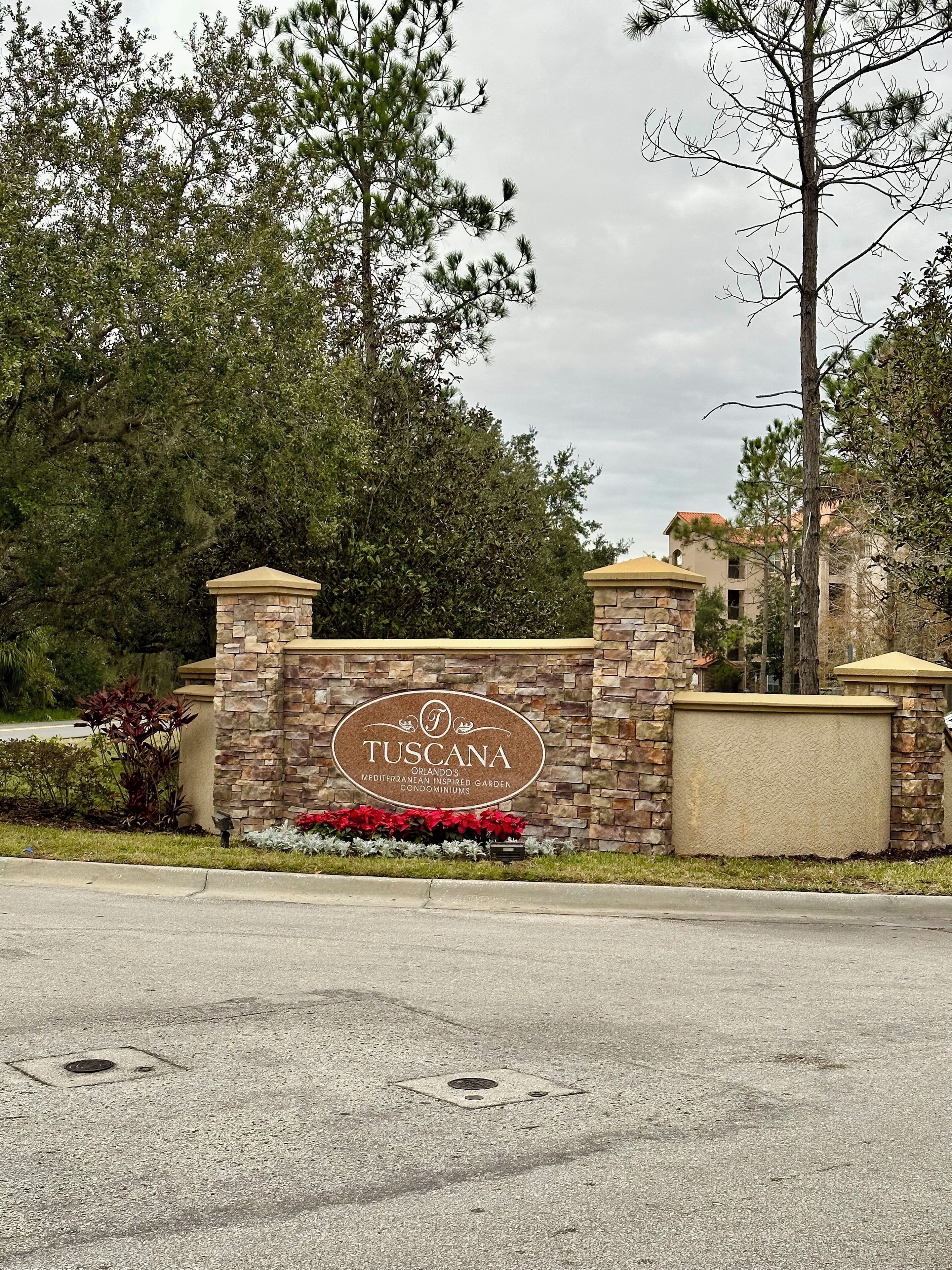 Mural de pedra com uma placa indicando 'TUSCANA ORLANDO'S MEDITERRANEAN INSPIRED GARDEN CONDOMINIUMS'.