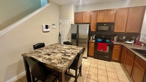 Cocina compacta con una mesa, sillas, refrigerador, microondas, estufa y armarios.