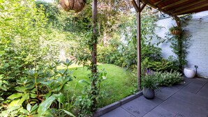 A covered patio area with hanging planters, a grassy garden, and a white brick wall.