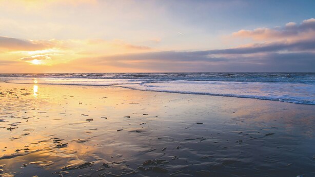 A beach with a sunset, waves, and a clear sky.