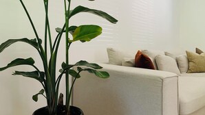 A living room with a large potted plant, a beige sofa, and a wooden floor.