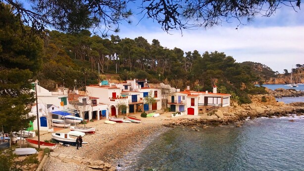 A coastal village with white buildings, a rocky beach, and boats.