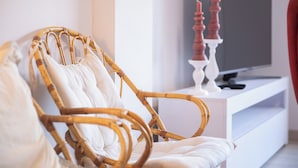 A wicker chair with white cushions in a modern living room with a white entertainment unit and a flat-screen TV.
