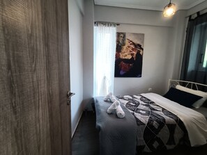 Un dormitorio con cama, un banco, un cuadro y una ventana con cortinas.