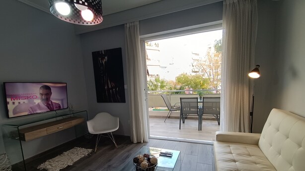 Una sala de estar moderna con un televisor de pantalla plana, un sofá blanco, una mesa de centro de vidrio y un comedor con mesa y sillas.
