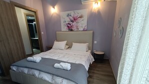 Un dormitorio con cama, almohadas, una mesita de noche, una lámpara de pared y un cuadro con motivos florales.