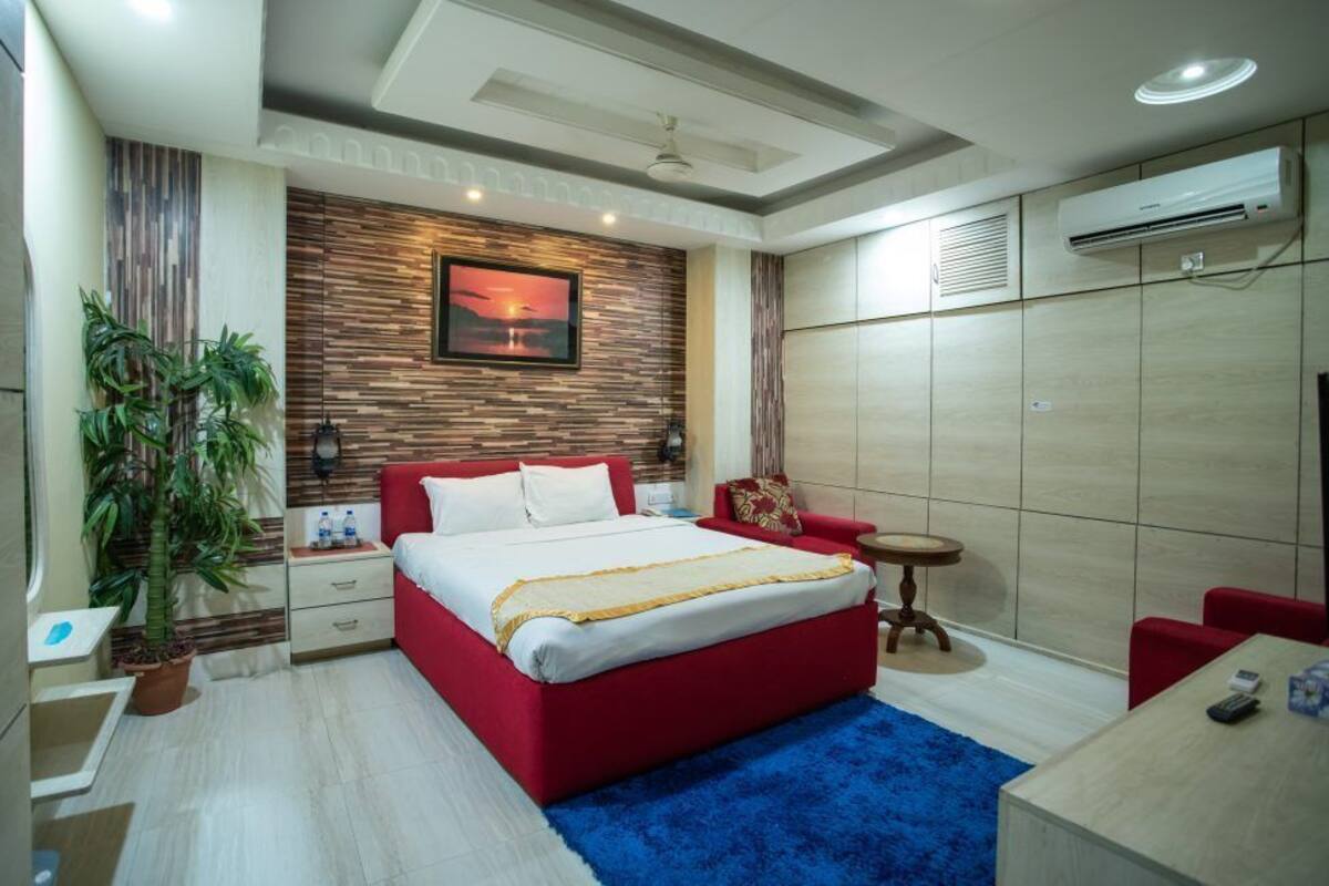 A modern bedroom with a red bed, a large window, a potted plant, and a blue rug.