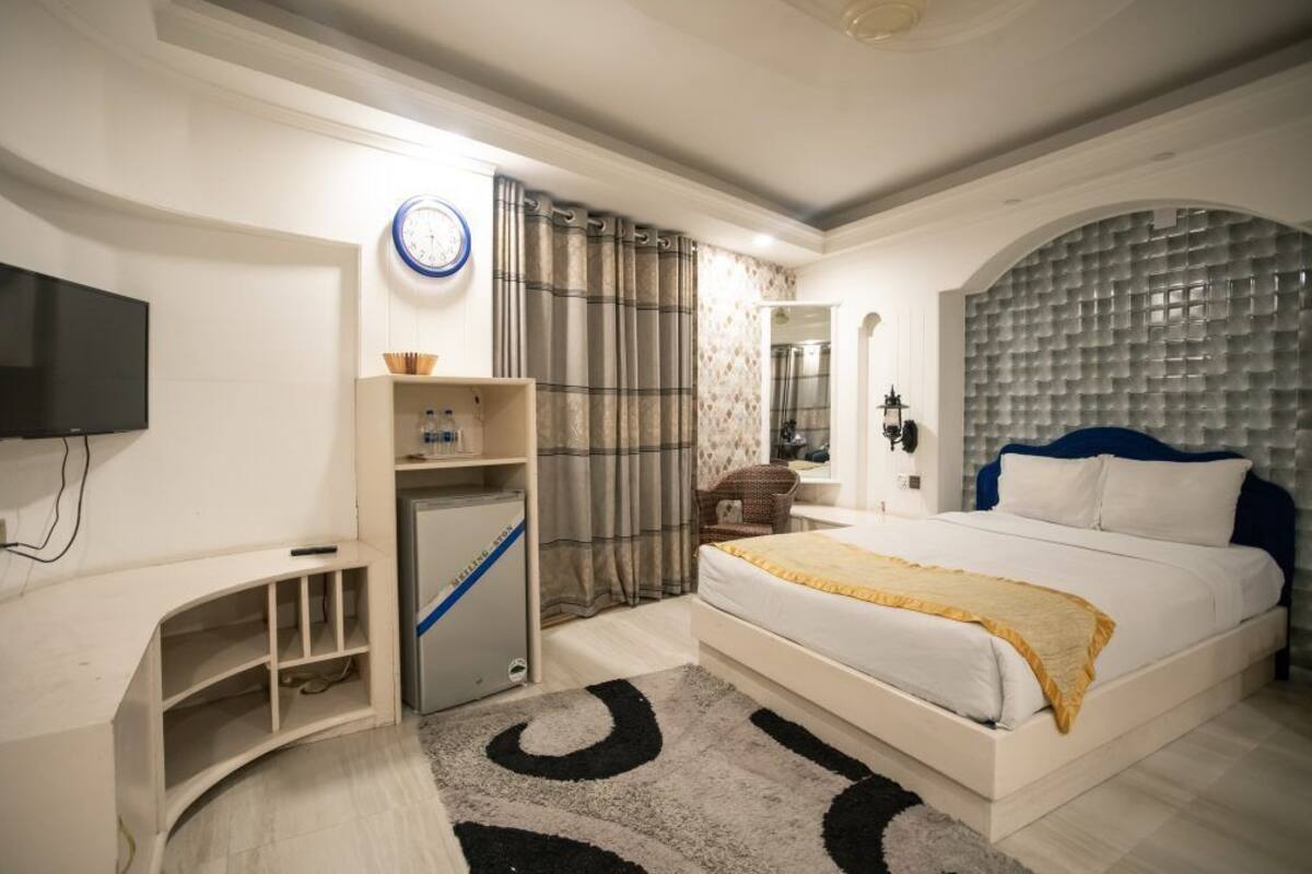 A bedroom with a bed, a desk, a television, a clock, and a bathroom mirror.