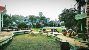 A park with a fountain, seating areas, and a large building in the background. - The Silver Castle  (Mymensingh)