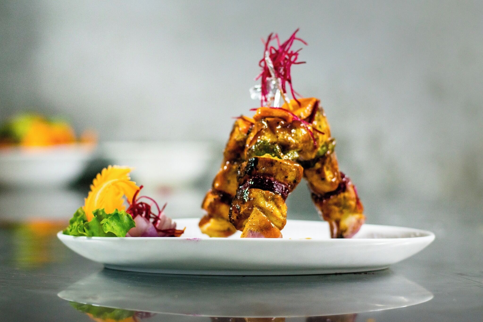A plate with grilled chicken skewers garnished with vegetables and a decorative element.