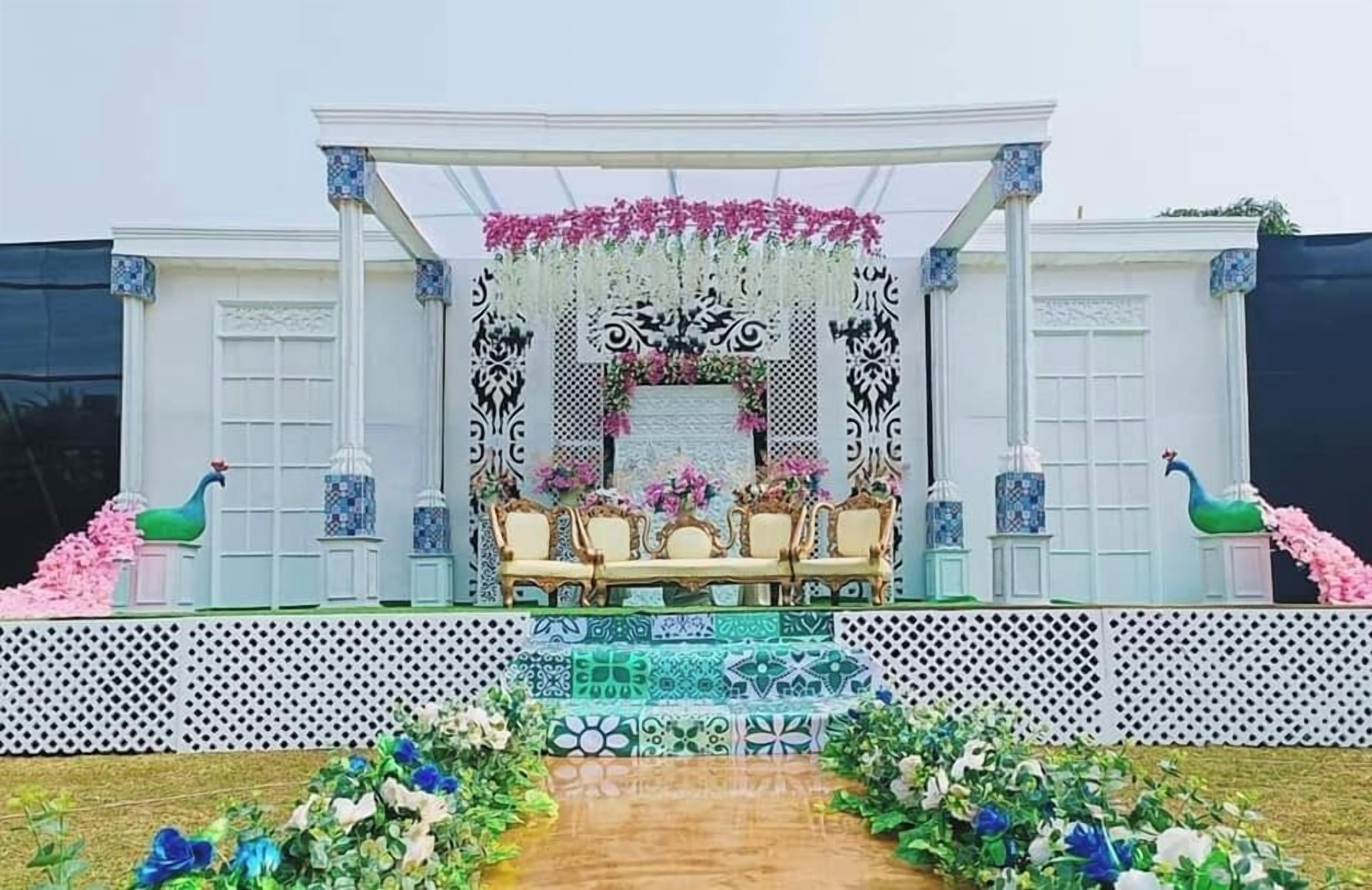 Un escenario con fondo blanco, decoraciones florales y disposición de asientos.