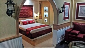 A hotel room with a large bed, a red upholstered headboard, two wall-mounted lamps, a red sofa, and a glass coffee table. - The Silver Castle  (Mymensingh)
