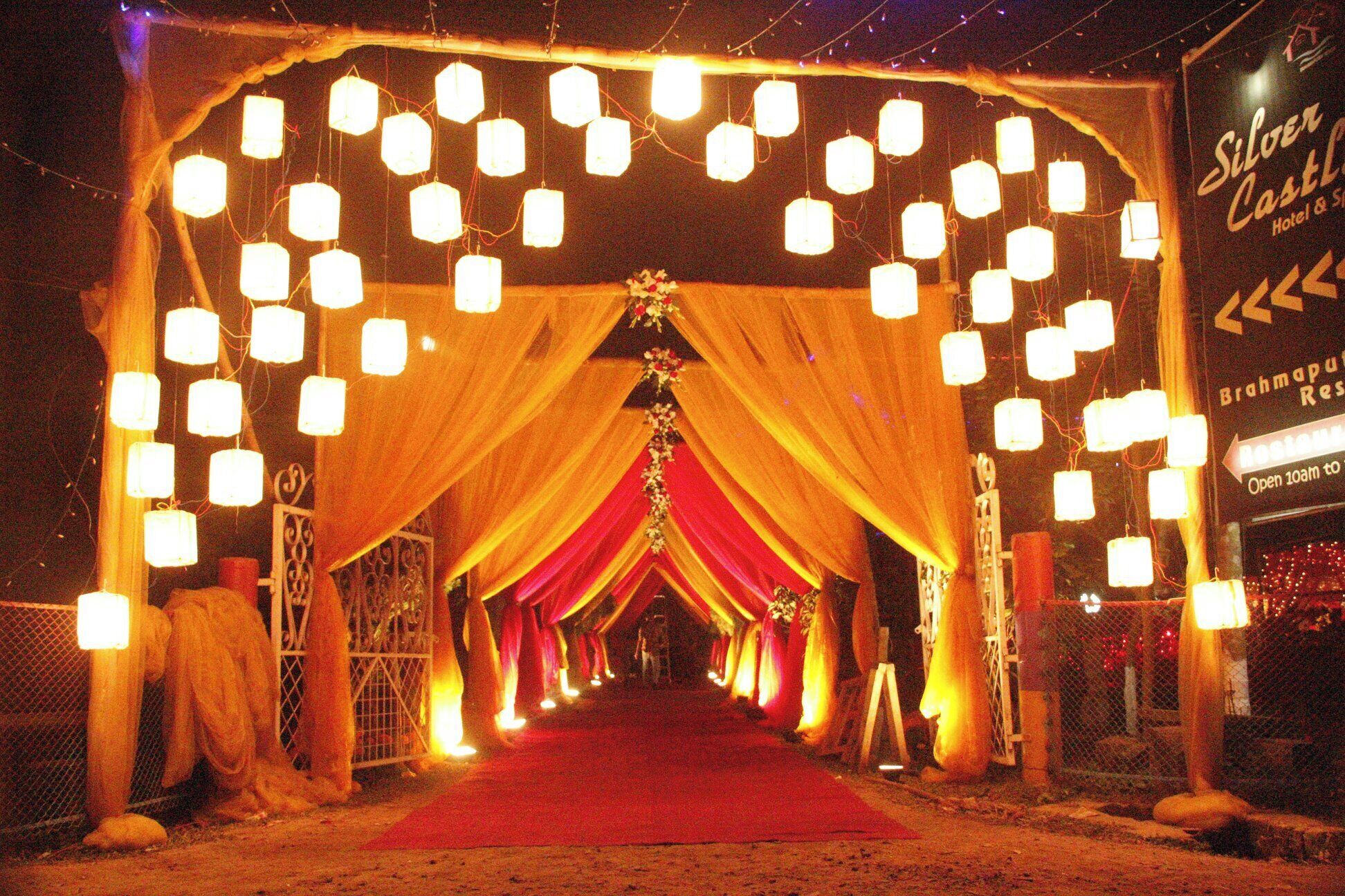 A decorated entrance with hanging lights and draped fabric, leading to a building with a sign reading "Silver Castle Hotel & Suites".