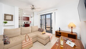 Uma sala de estar com sofá, mesa lateral de madeira com luminária e vista para o exterior por uma porta de correr de vidro.