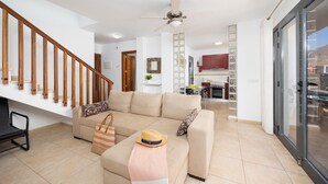 Uma sala de estar espaçosa com escada de madeira, um conjunto de sofás, um espaço para refeições e uma cozinha com armários vermelhos.