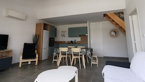 Una sala moderna con sofá, una mesa de comedor con sillas, una zona de cocina con armarios y estufa, y una escalera que conduce a otro nivel.