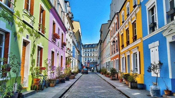 A narrow cobblestone street lined with colorful buildings, each with a visible door and window.
