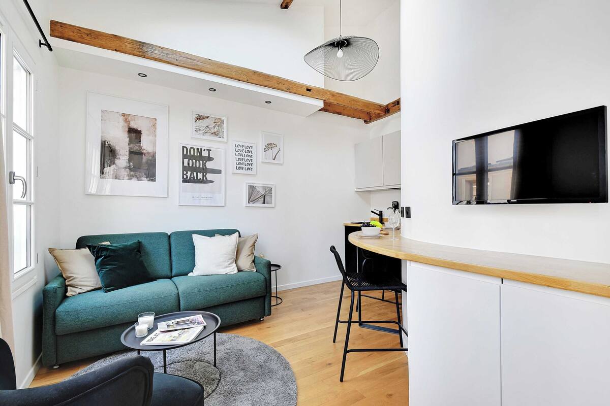 A modern living room with a green sofa, a coffee table, and a dining area with a wooden countertop and chairs.
