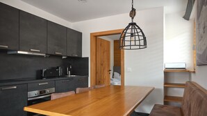 Una cocina moderna con armarios oscuros, una mesa de comedor de madera y una lámpara colgante.
