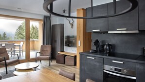 A modern kitchen with dark cabinetry, a wooden dining table, and a large window overlooking a balcony. - 59111 Bartgeier 111 T (Gargellen)