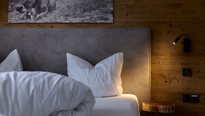 A neatly made bed with white bedding, a grey headboard, and a wooden wall with a mounted picture. - 59111 Bartgeier 111 T (Gargellen)