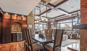 A spacious dining area with a wooden table and chairs, a fireplace, and large windows offering views of the surrounding landscape.