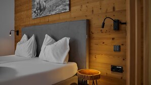 Un dormitorio moderno con pared de madera, cabecero gris, ropa de cama blanca y un taburete de madera pequeño.