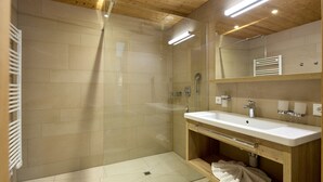Une salle de bain moderne dotée d’une douche à parois de verre, d’un meuble-lavabo en bois et d’un miroir placé au-dessus du meuble-lavabo.