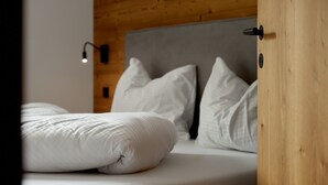 Un lit bien fait, avec une literie blanche, dans une pièce aux murs en bois et dotée d’une tête de lit moderne.