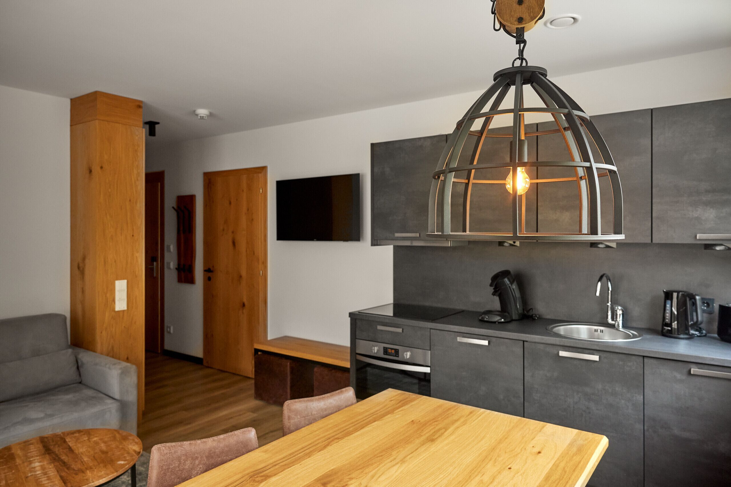 Une cuisine moderne avec une table à manger en bois, des meubles de rangement gris et un luminaire suspendu.