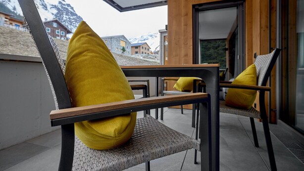 A modern outdoor seating area with wicker chairs and yellow cushions, overlooking a mountainous landscape. - 59115 Fels-Schwalbe 115 (Gargellen)