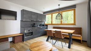 A modern kitchen with grey cabinets, a wooden dining table, and a bench. - 59115 Fels-Schwalbe 115 (Gargellen)