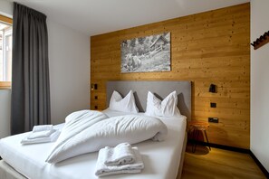 Un lit bien fait, avec du linge de lit blanc et des oreillers, un mur en bois orné d’un tableau, et un petit tabouret en bois.