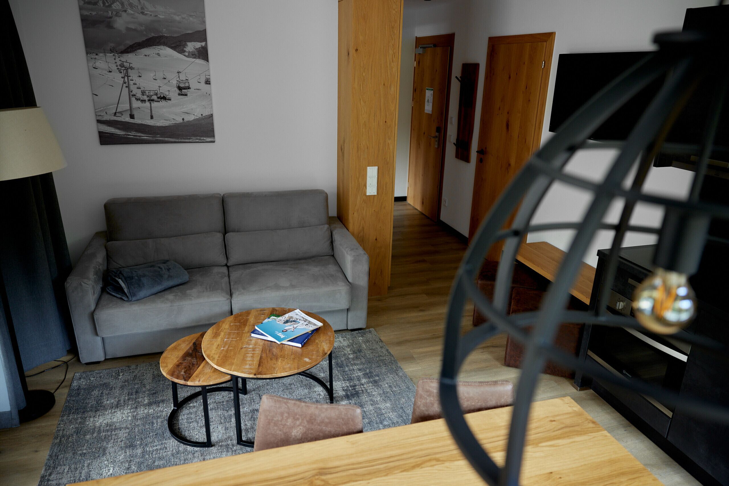 Un salon avec un canapé gris, une table basse en bois, un meuble TV noir et un escalier menant à une autre pièce.