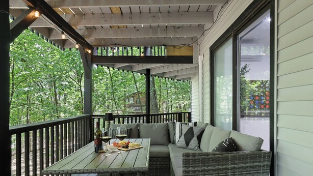 An outdoor seating area with a table, chairs, and a sofa, overlooking a forested area. - Poconos Chatham Continental - Hot Tub & Fire Pit! (Bushkill)