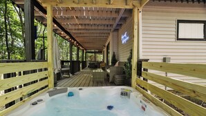 En træterrasse med jacuzzi, udendørs møbler og et overdækket område med en neonreklame.