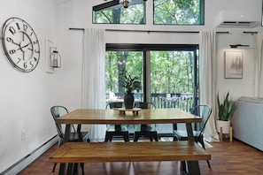 A dining area with a wooden table, chairs, a clock, and a view of trees through large windows. - Poconos Chatham Continental - Hot Tub & Fire Pit (Bushkill)