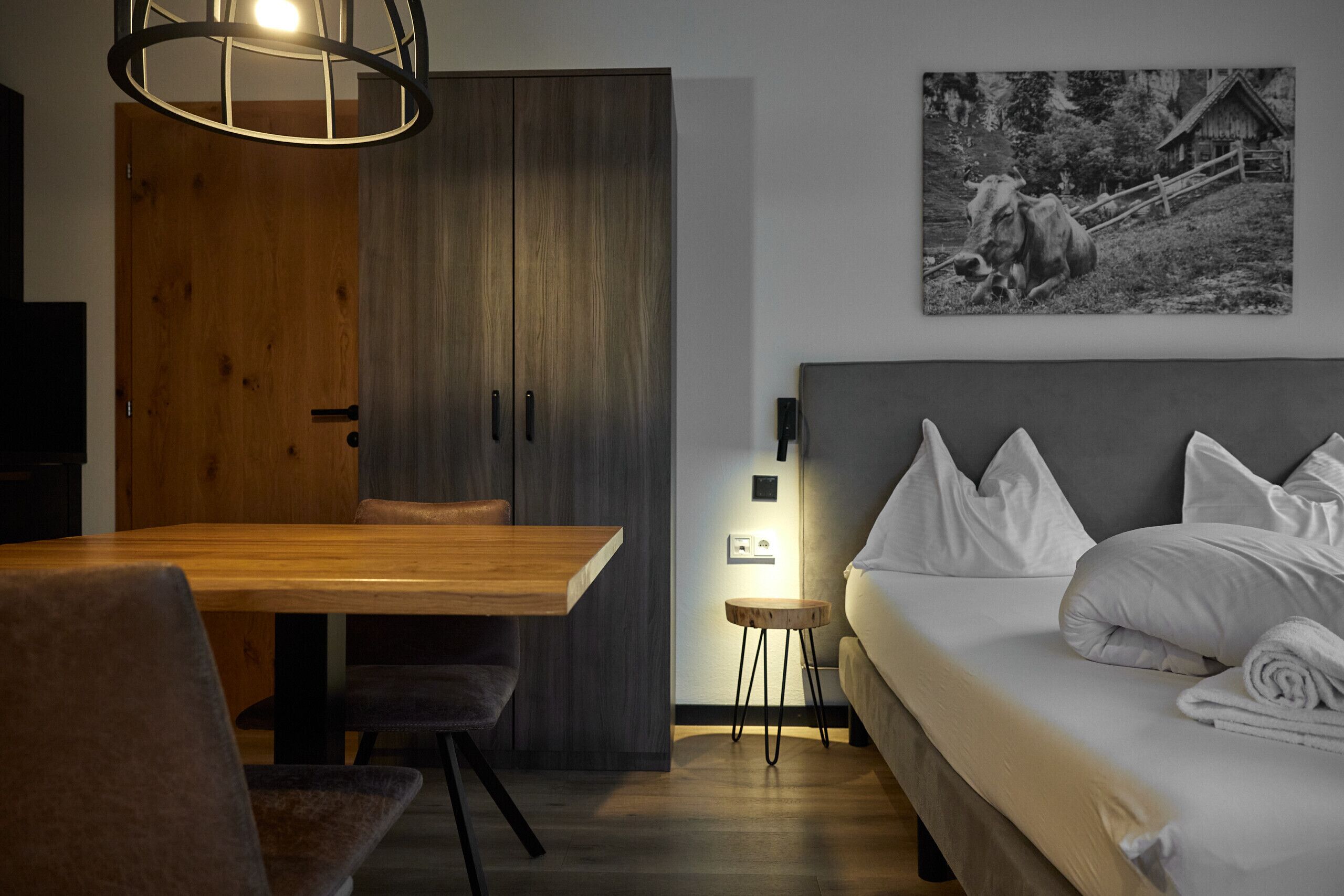 A modern bedroom with a wooden dining table, a sofa, and a bed with white bedding.