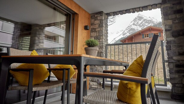 Ein Balkon mit Tisch, Stühlen, einem Blumentopf und Blick auf einen Berg.