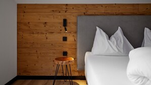 Ein modernes Schlafzimmer mit einer Holzwandverkleidung, einem grauen Kopfteil, weißer Bettwäsche und einem kleinen Holzschemel.