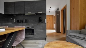 A modern kitchen with dark cabinets, a wooden dining table, and a grey sofa in a living area. - 59217 Wanderfalke 217 T (Gargellen)