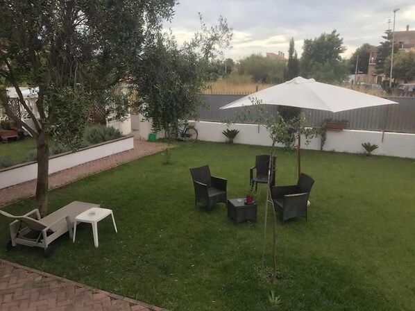 A backyard with a lawn, a white umbrella, and outdoor furniture. - Alloggio Turistico (Fiumicino)