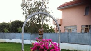 A circular planter with a metal arch and a birdhouse, containing pink flowers and green foliage, placed on a stone-paved area. - Alloggio Turistico (Fiumicino)