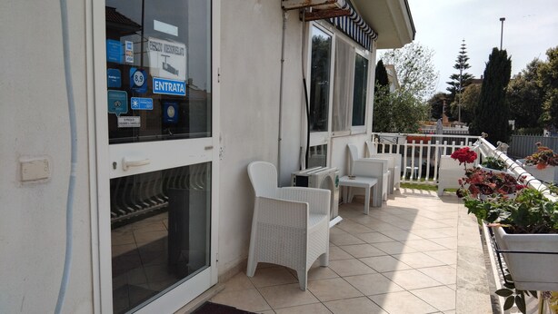 A hotel entrance with a glass door, a sign indicating room availability, and a patio area with outdoor furniture and potted plants. - Alloggio Turistico (Fiumicino)